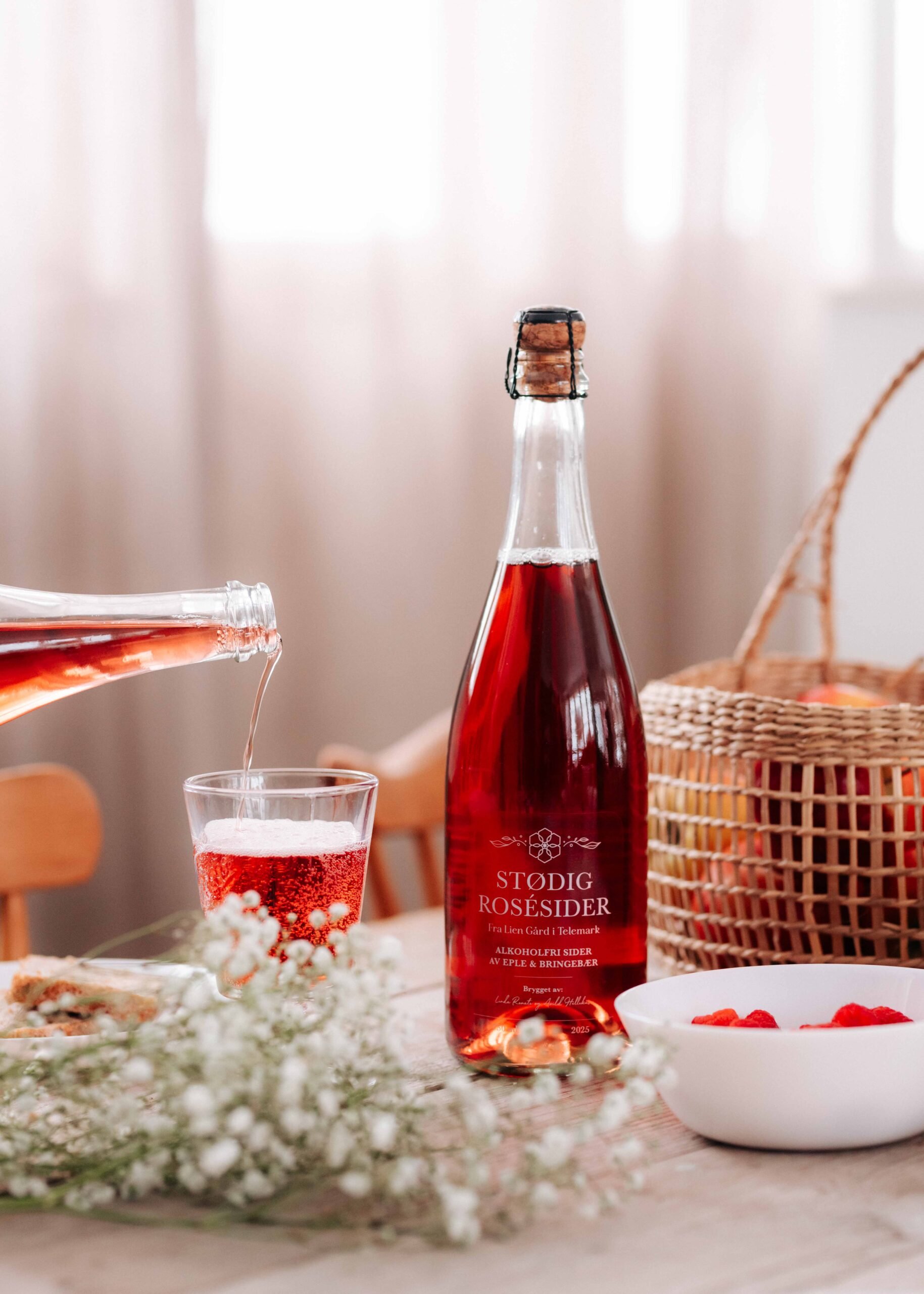 Flaske med Stødig rosésider, servert i glass, med bær og blomster på bordet. Perfekt for en hyggelig samling.