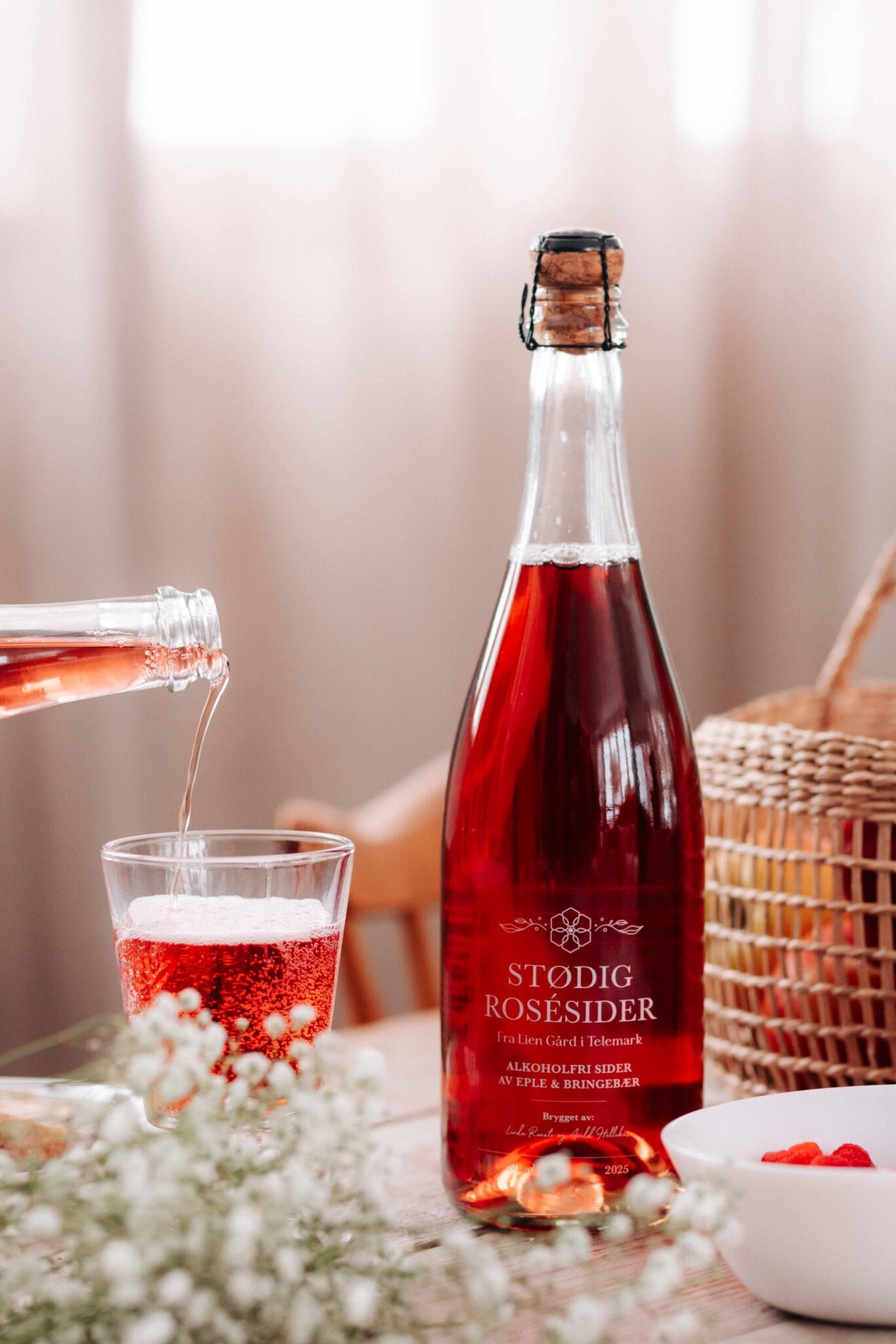 Flaske med rosésider og glass med bobler, servert med friske bær på bordet i solfylt rom.